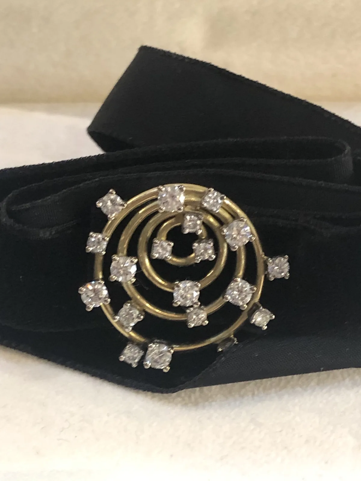 A circular gold brooch set with diamonds on a velvet ribbon