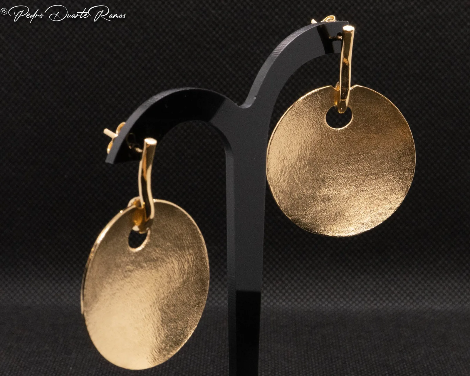 A pair of hammered gold disc earrings, photographed on black