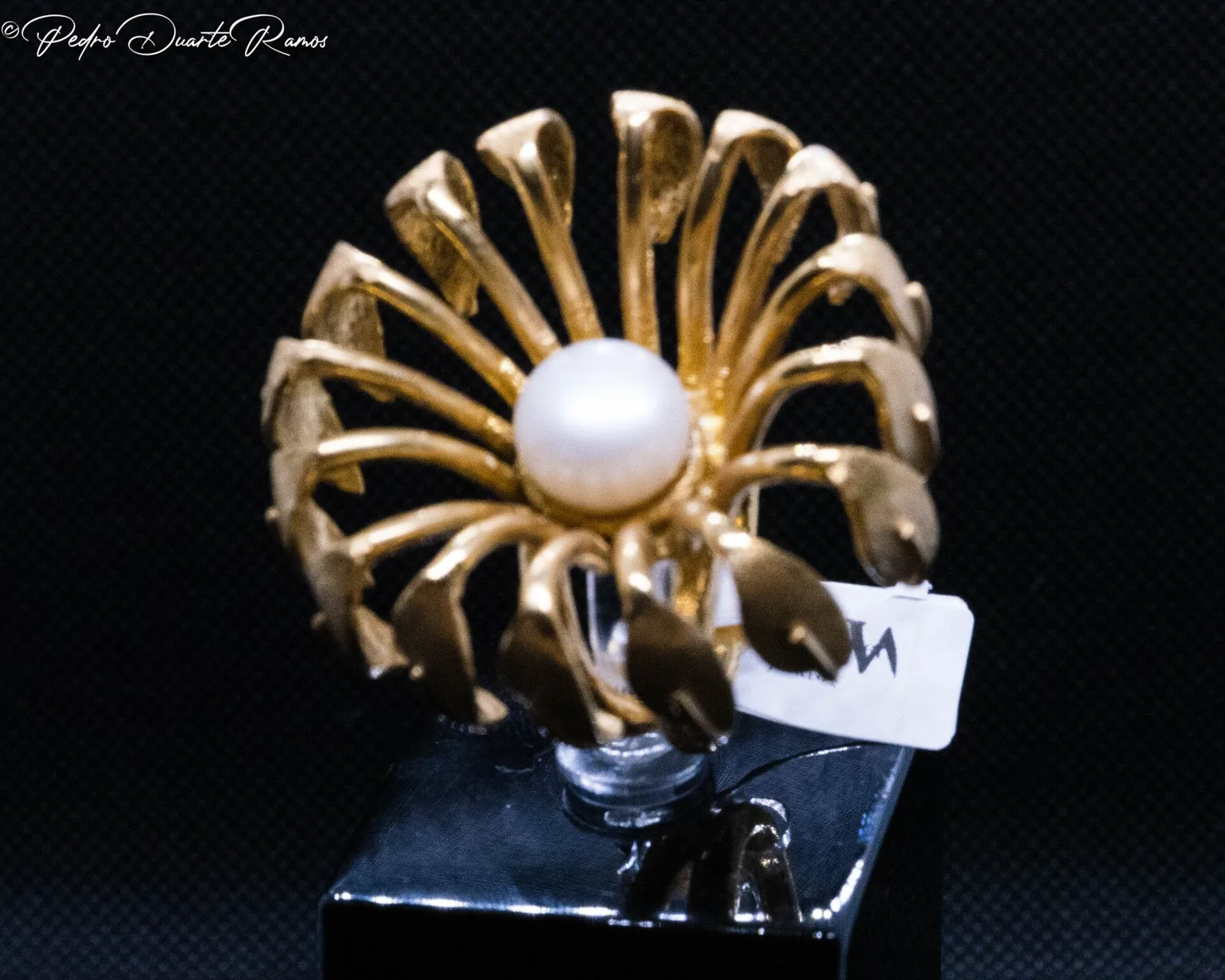 A gold flower brooch with a pearl centre, photographed on black